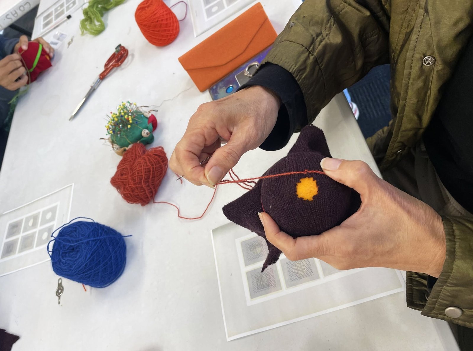 Hands mending a knitted garment with colourful yarn